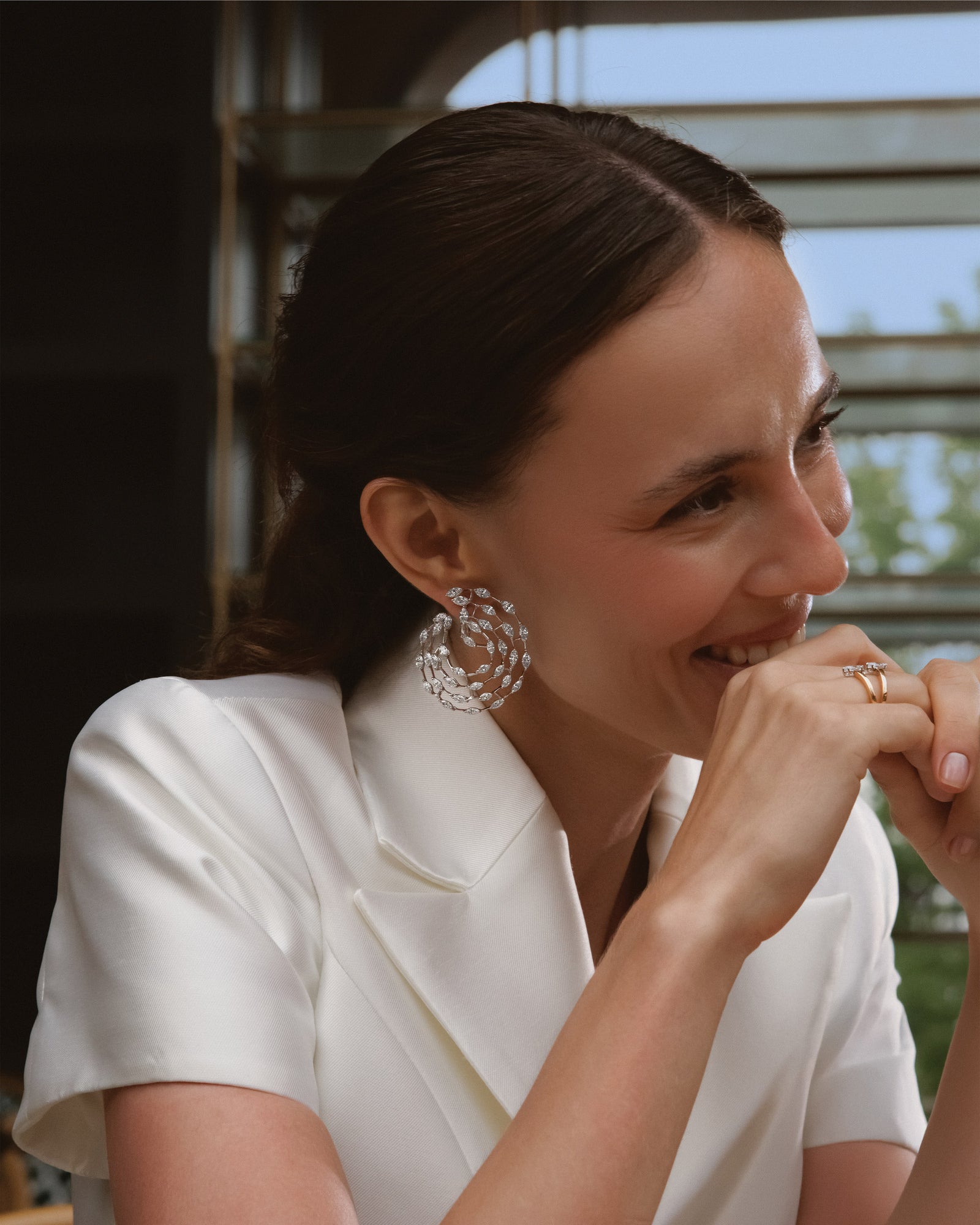 At a café table she laughs, chin resting on her hand, diamond earrings on.