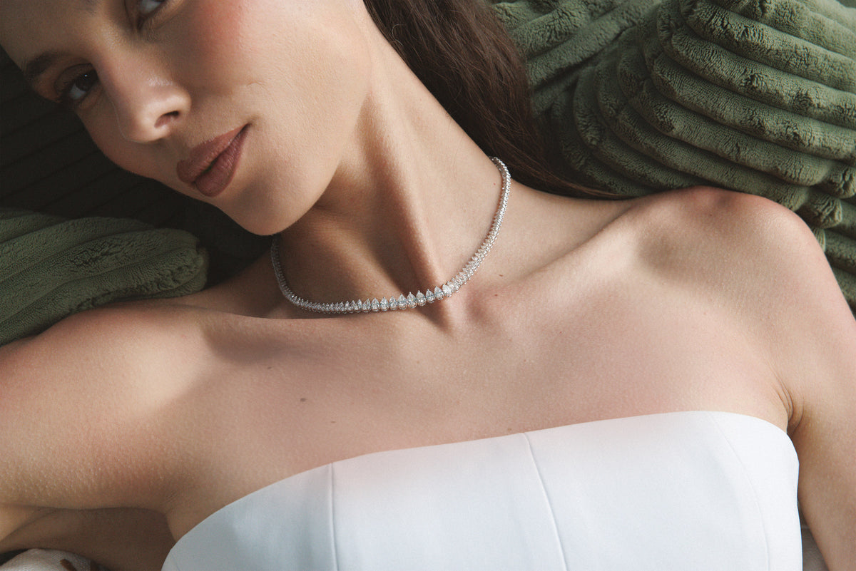 She rests against a green cushion in a white dress, a diamond rivière at her throat.