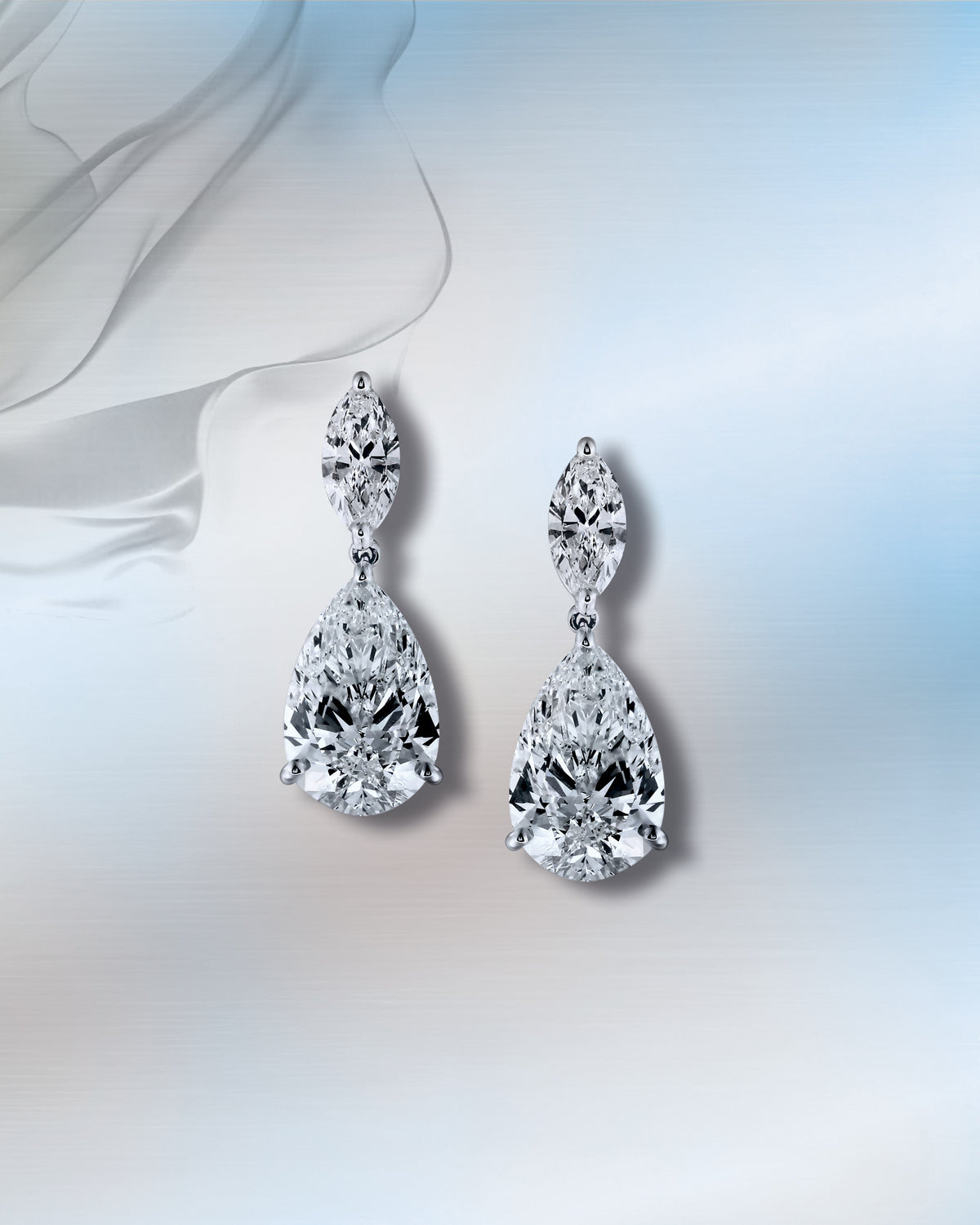 A pair of pear-shaped diamond drop earrings, on pale blue silk.