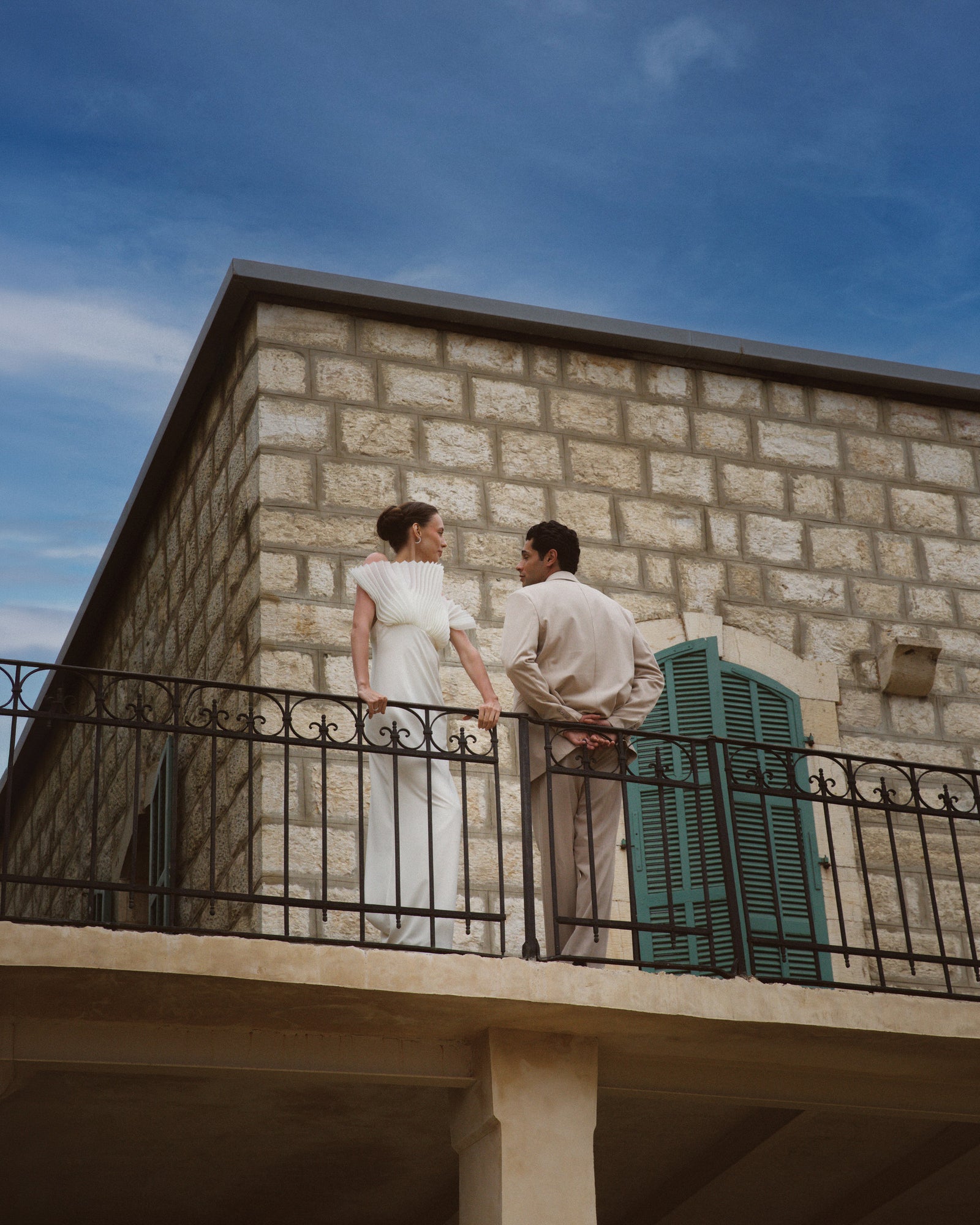 The two of them on the balcony of a stone house, under a clear sky.